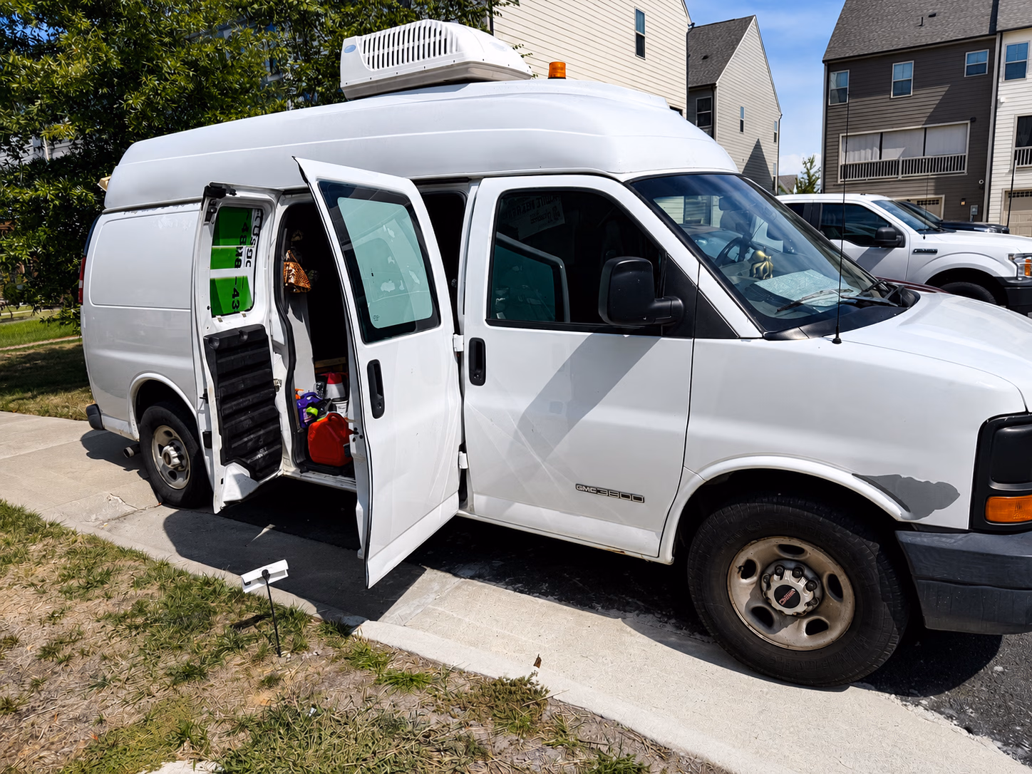 White GMC 3500 van with doors open, parked on a residential street on a sunny day.