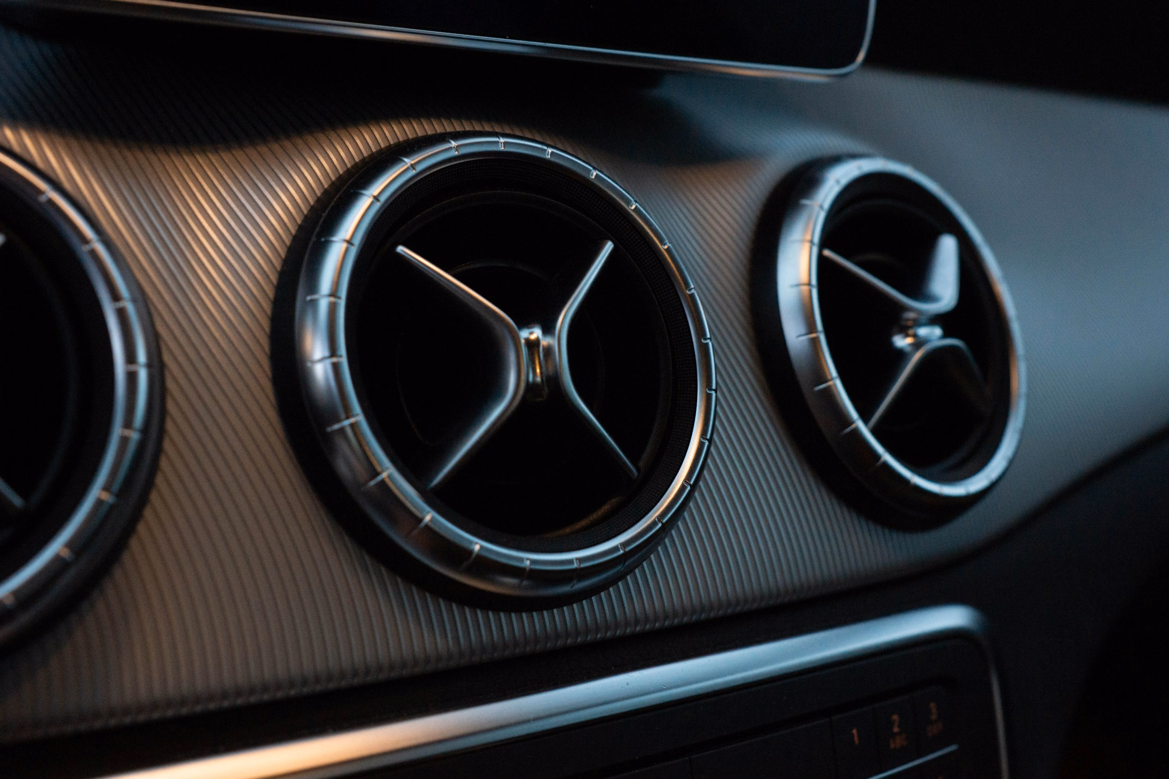 Close-up of three circular car air conditioning vents on a textured dashboard.