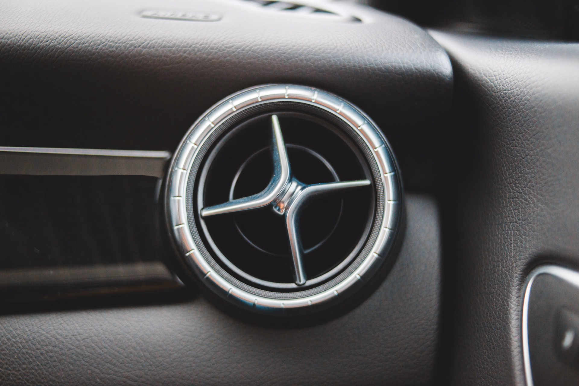 Close-up of a round car air vent with a silver trim and three metal fins inside.