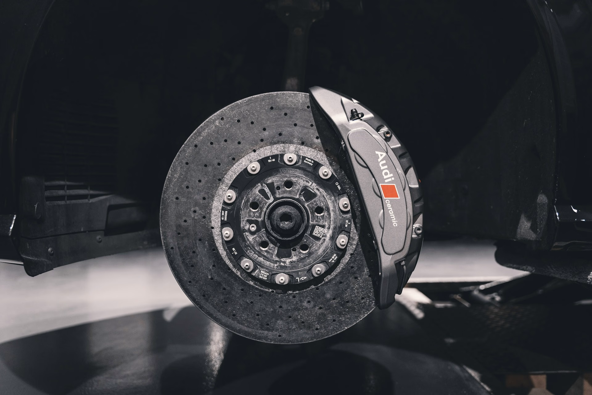 Close-up of an Audi ceramic brake rotor and caliper on a black car without the wheel.