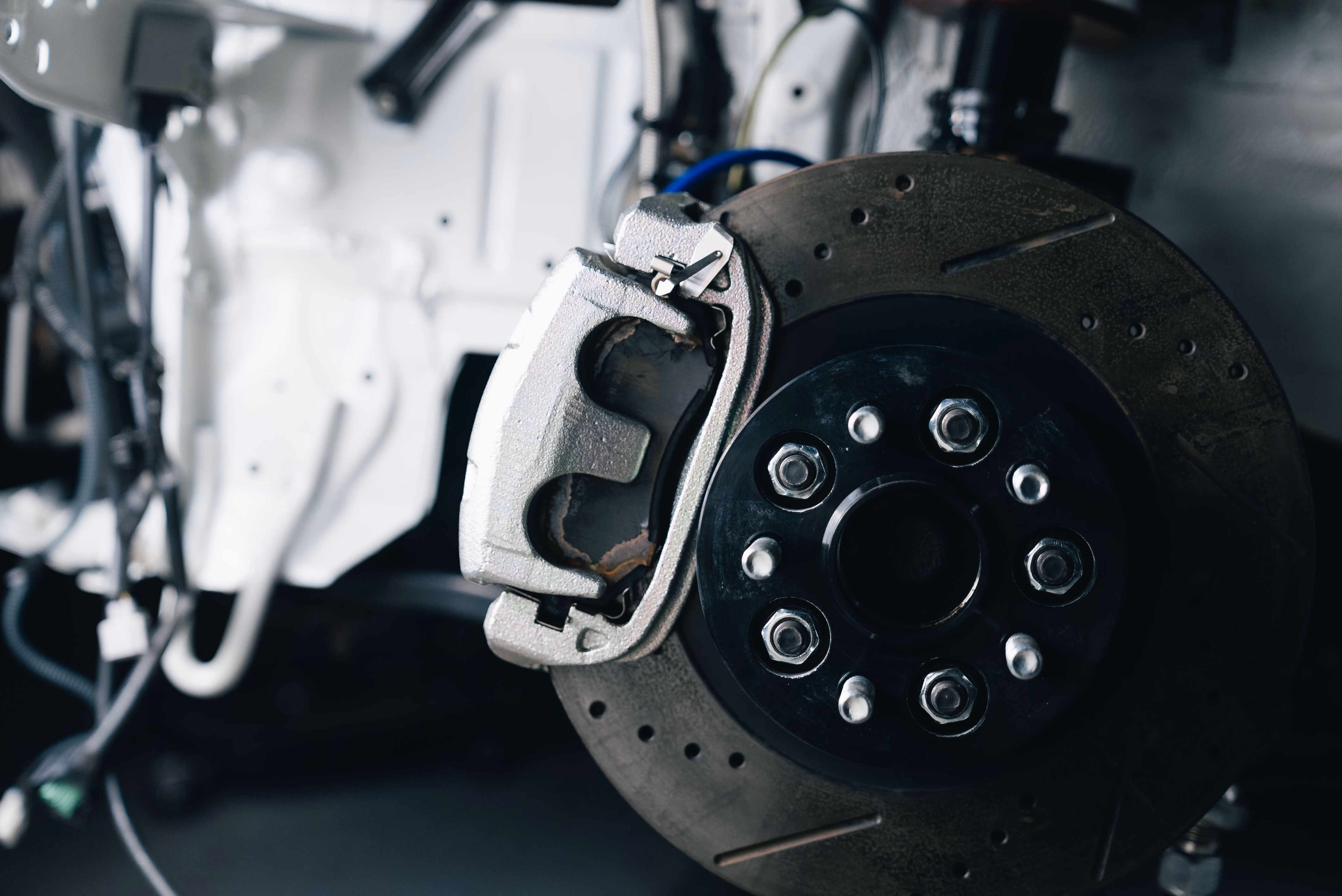 Close-up of a car disc brake assembly with caliper and drilled rotor in a repair setting.