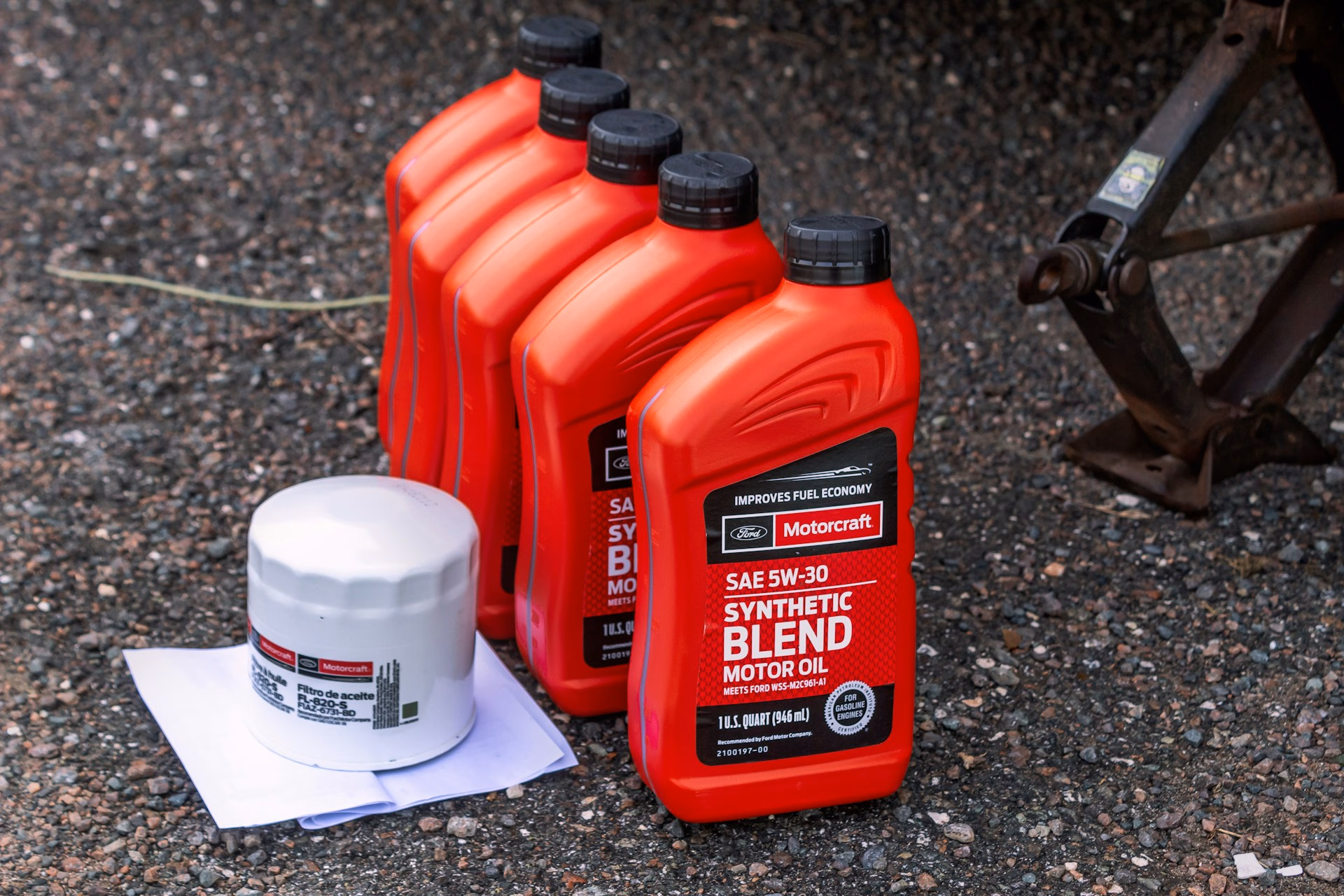 Five red Motorcraft synthetic blend motor oil containers and a white oil filter on gravel.
