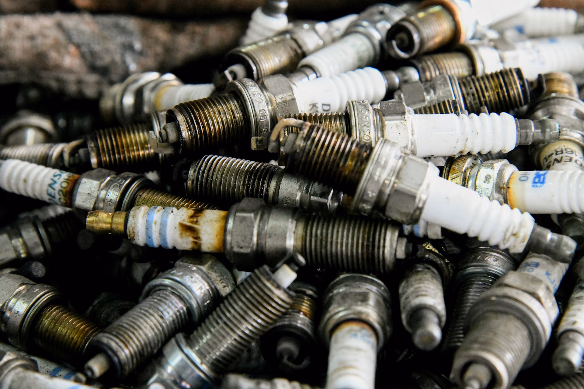 Pile of used spark plugs with white ceramic insulators and metal threaded ends.