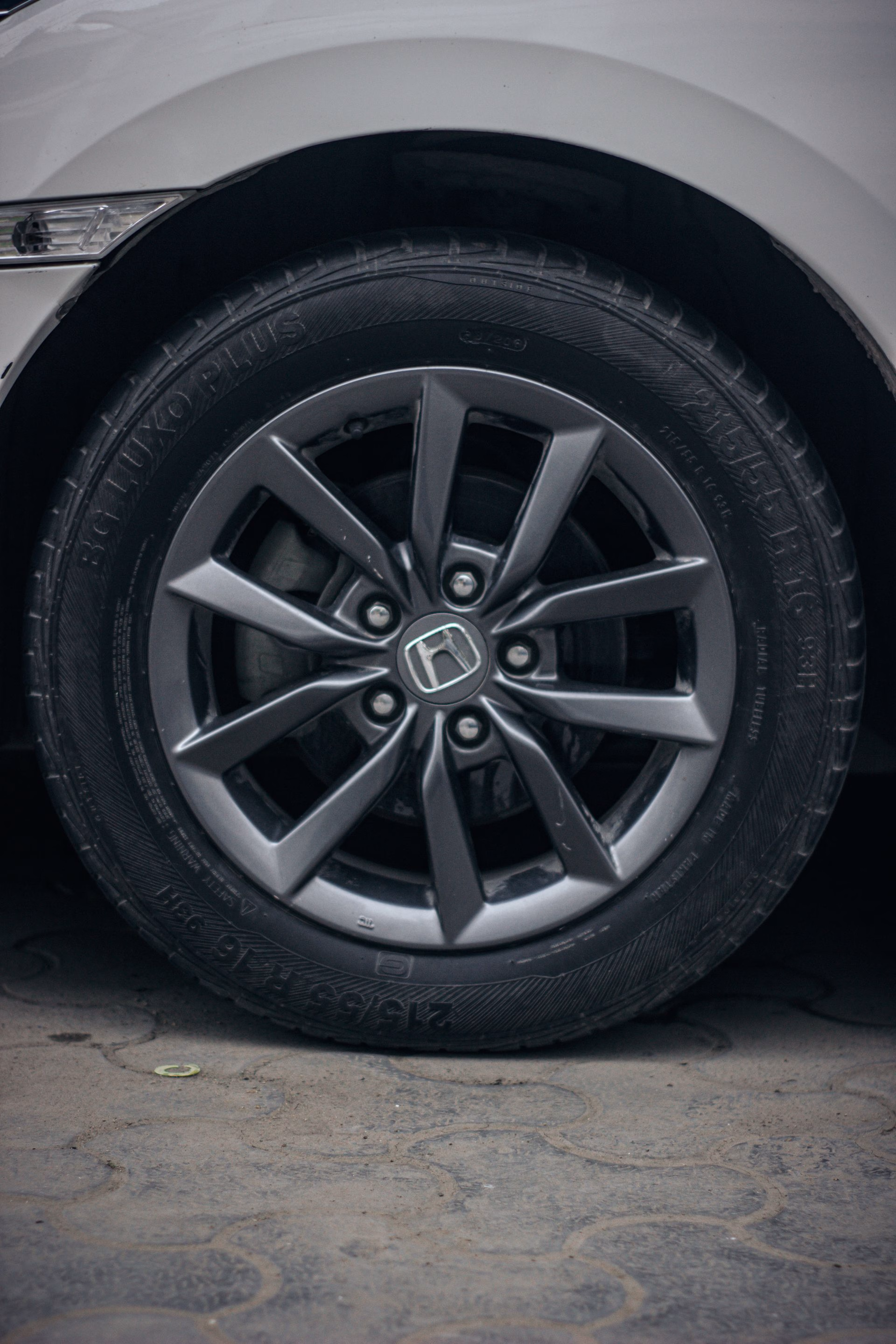 Close-up of a black Honda car tire and alloy wheel on a paved surface.